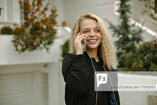 Glückliche blonde Frau  die im Vorgarten mit ihrem Handy telefoniert