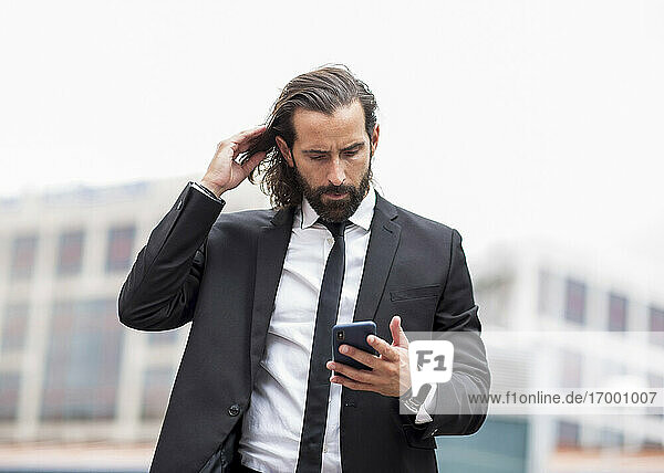 Portrait of bearded businessman standing outdoors with smart phone in hand