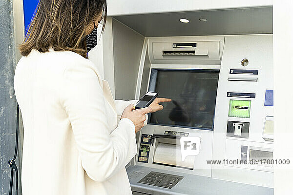 Unternehmerin beim Geldabheben am Geldautomaten während der COVID-19
