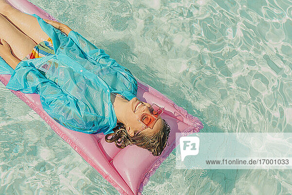 Woman wearing blue rain coat relaxing on pink airbed in swimming pool