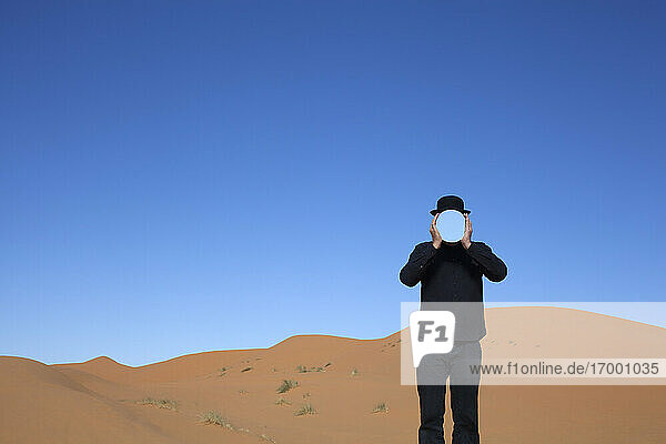 Marokko  Merzouga  Erg Chebbi  Mann mit Melone  der sich in einer Wüstendüne einen Spiegel vor das Gesicht hält