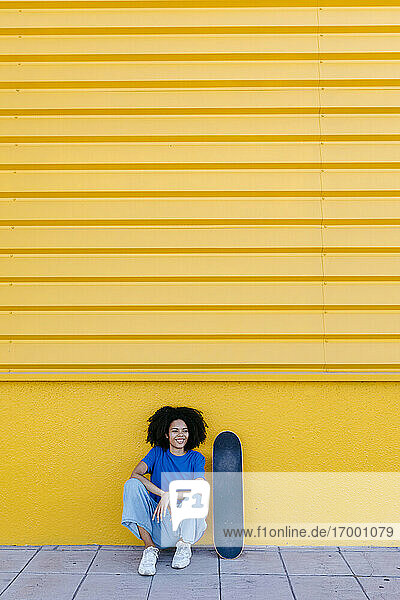 Junge Frau mit Skateboard vor einer gelben Geldbörse sitzend