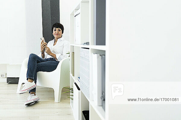 Geschäftsfrau in Bürosessel sitzend mit Smartphone in den Händen