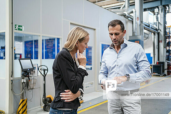 Businessman explaining female colleague over digital tablet while standing at factory