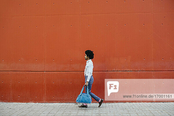 Mann mit Tasche auf der Straße vor einer roten Wand