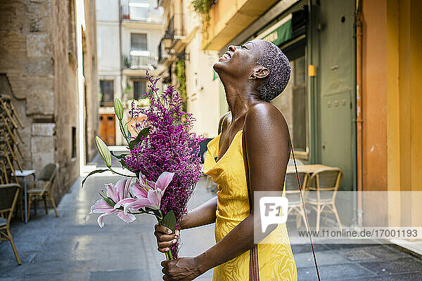 Fröhliche Frau mit Blumen vor einem Straßencafé in der Stadt