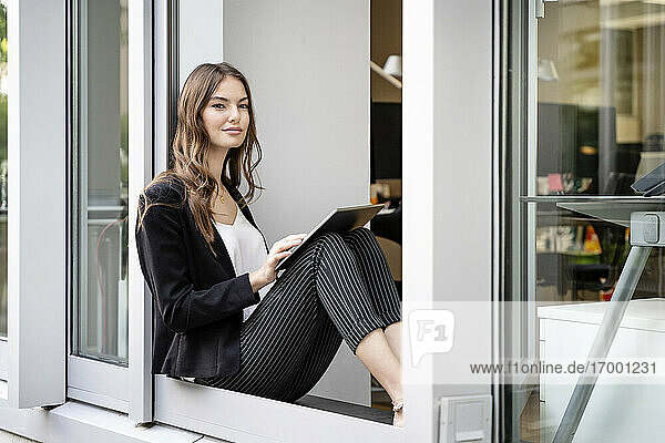 Young businesswoman using digital tablet while sitting at office door