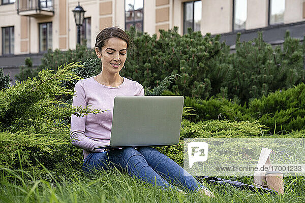 Junge Geschäftsfrau mit Laptop im Park sitzend