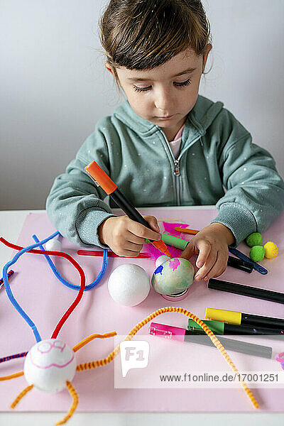 Girl coloring styrofoam ball with sketch pen on table