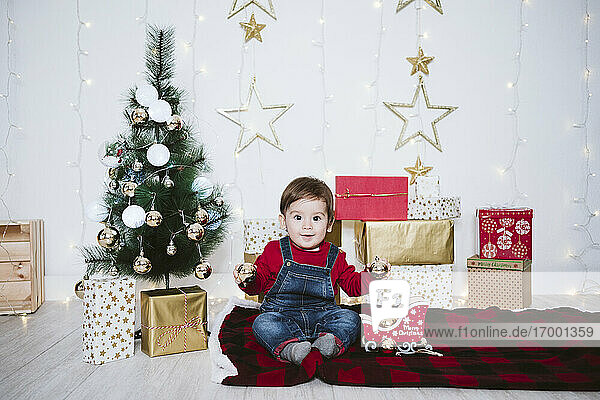 Niedlicher Junge spielt mit einer Weihnachtskugel  während er zu Hause auf einer Decke sitzt