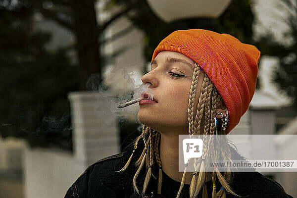 Junge Frau in orangefarbenem Strickkleid raucht Zigarette