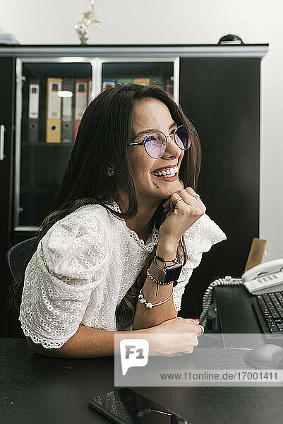 Geschäftsfrau lächelt  während sie mit der Hand am Kinn im Büro sitzt