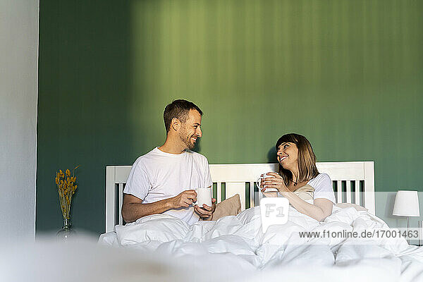 Lächelndes Paar beim Kaffee trinken auf dem Bett zu Hause