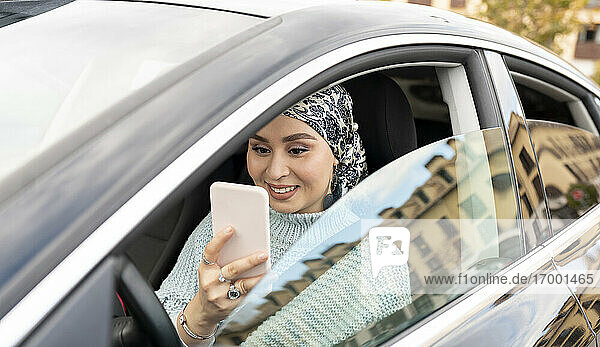 Frau mit Kopftuch  die ein Mobiltelefon benutzt  während sie in einem Auto in der Stadt sitzt