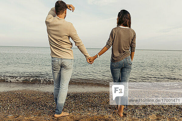 Junges Paar schaut auf das Meer und steht auf Sand