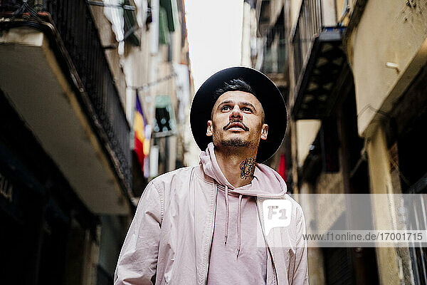 Nachdenklicher stilvoller Mann  der einen Hut trägt  während er vor einem Gebäude in der Stadt steht