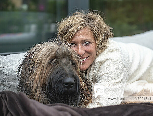 Lächelnde Frau  die ihren Hund umarmt  während sie auf dem Sofa im Hinterhof sitzt