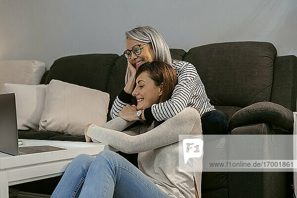 Lächelnde Mutter und Tochter  die zu Hause am Laptop sitzen