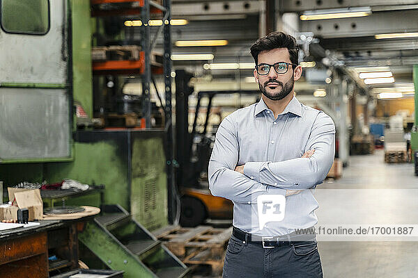 Confident businessman with arms crossed standing at manufacturing industry