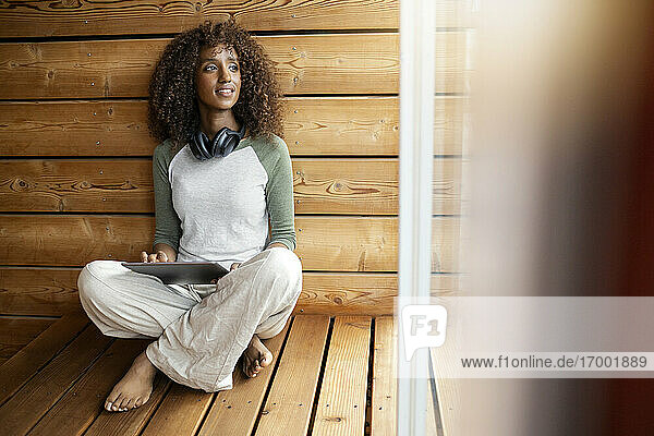 Frau mit digitalem Tablet  die zu Hause im Schneidersitz sitzt