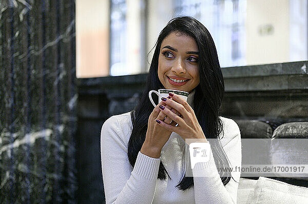 Beautiful businesswoman holding coffee cup while looking away in cafe