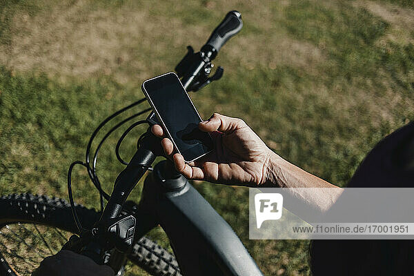 Frau  die ein Mobiltelefon benutzt  während sie in einem Park neben einem elektrischen Mountainbike steht