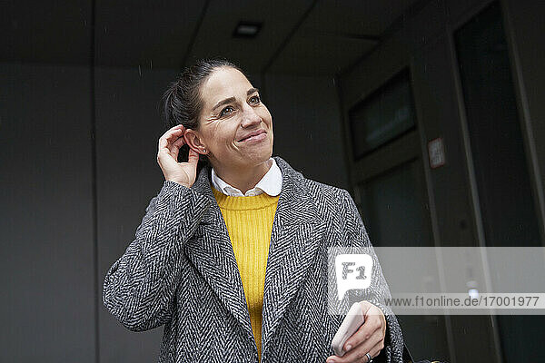 Lächelnde Geschäftsfrau  die im Freien stehend ein Mobiltelefon hält