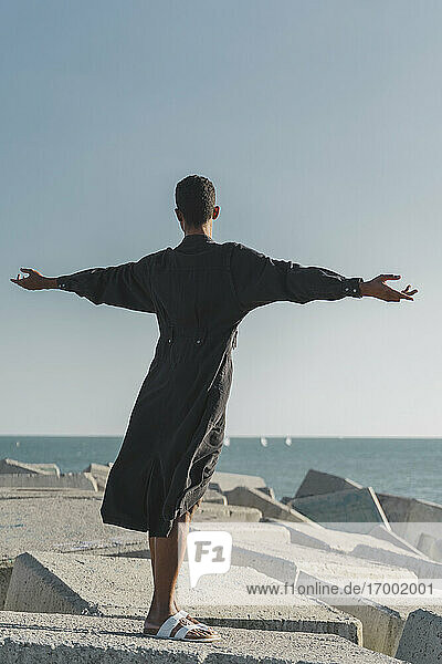 Junger Mann mit schwarzem Kaftan auf Betonblöcken an der Küste