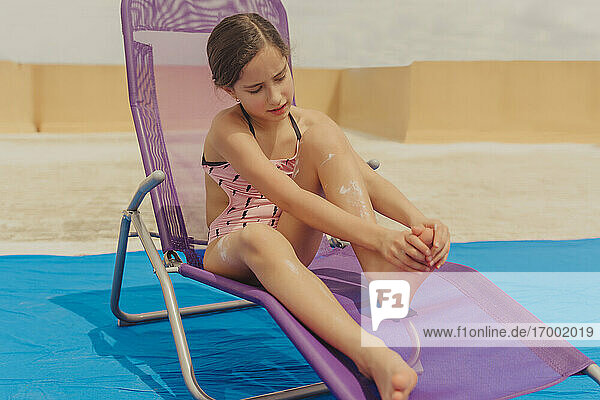 Porträt eines auf einer Sonnenliege sitzenden Mädchens  das sich mit Sonnencreme eincremt