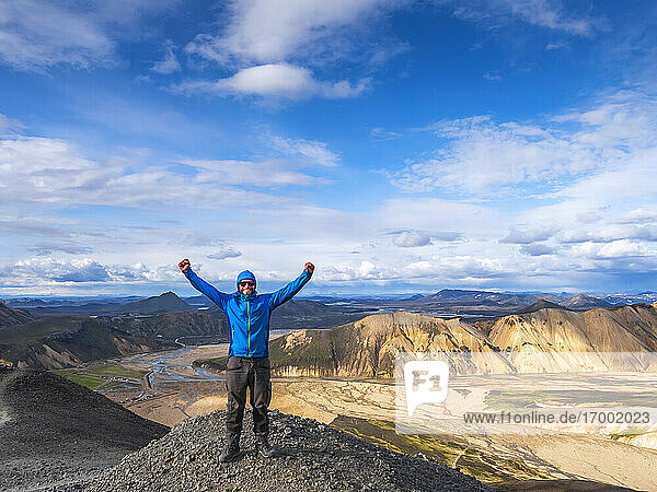 Hiker posing with raised arms on top of volcanic hill in Landmannalaugar