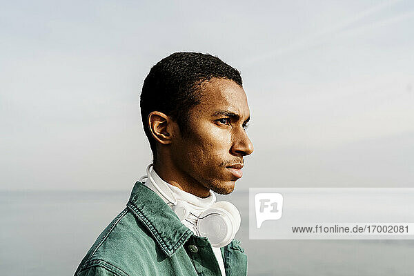 Junger Mann mit Kopfhörern blickt über Meer und Himmel hinweg