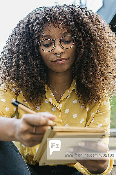 Young woman writing in book while sitting outdoors