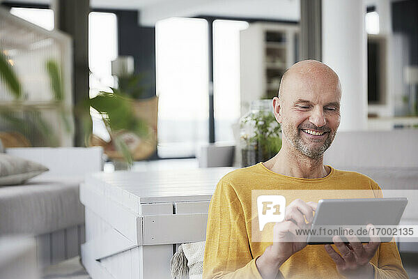 Lächelnder Mann  der ein digitales Tablet benutzt  während er zu Hause sitzt