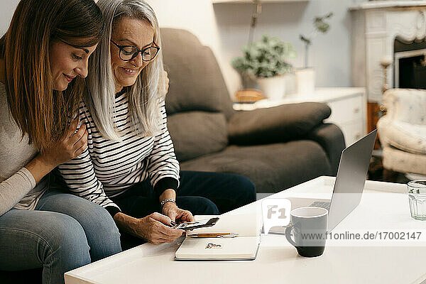 Lächelnde Mutter und Tochter  die ein Foto auf einem Buch über ein Mobiltelefon machen  während sie zu Hause sitzen