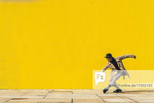 Junger Mann tanzt vor einer gelben Wand