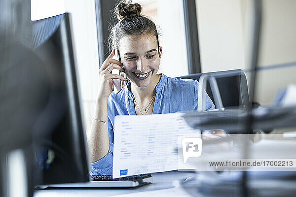 Geschäftsfrau  die im Büro sitzend mit einem Mobiltelefon telefoniert