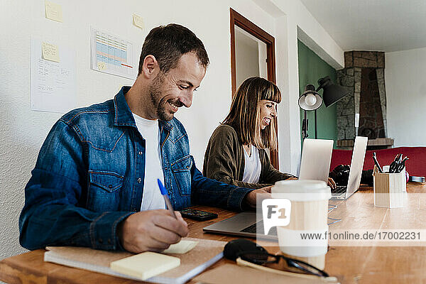 Lächelndes Geschäftspaar arbeitet am Laptop im Büro zu Hause