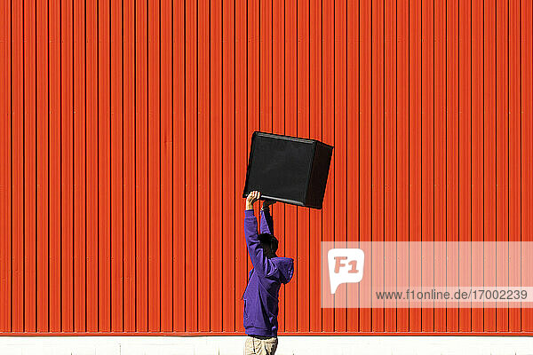 Young man carrying a box in front of a red wall