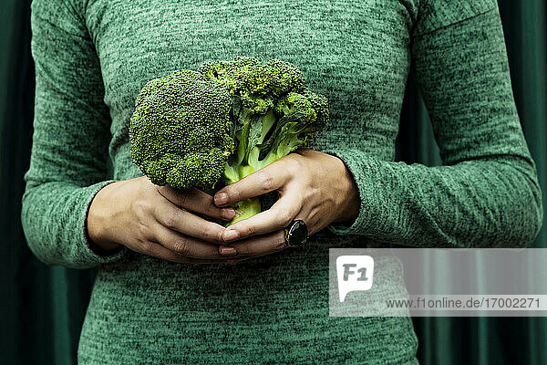 Midsection of woman standing with broccoli against curtain