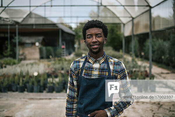 Smiling young farm worker standing against greenhouse