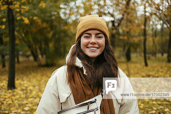 Glückliche junge Frau in warmer Kleidung im herbstlichen Park