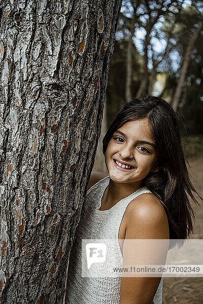 Smiling girl standing by tree trunk in forest during vacation