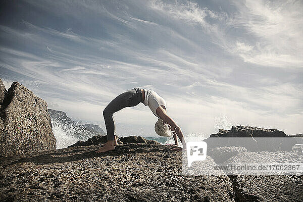 Biegsame Frau übt Brückenpose auf Felsformation am Strand