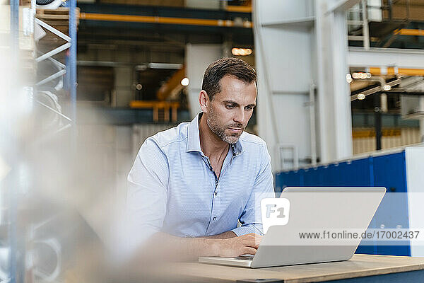 Male entrepreneur working on laptop while sitting in factory
