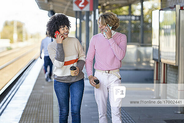 Glückliche Freunde  die am Bahnsteig mit ihren Handys telefonieren