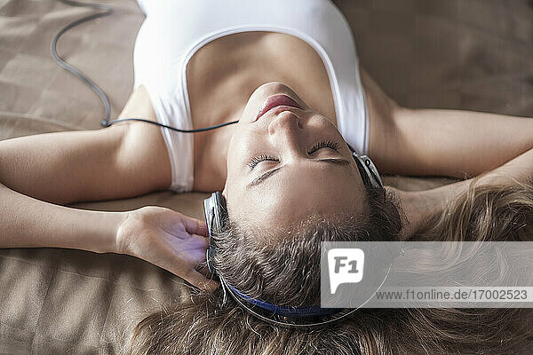 Nahaufnahme einer Frau  die beim Entspannen auf dem Bett über Kopfhörer Musik hört
