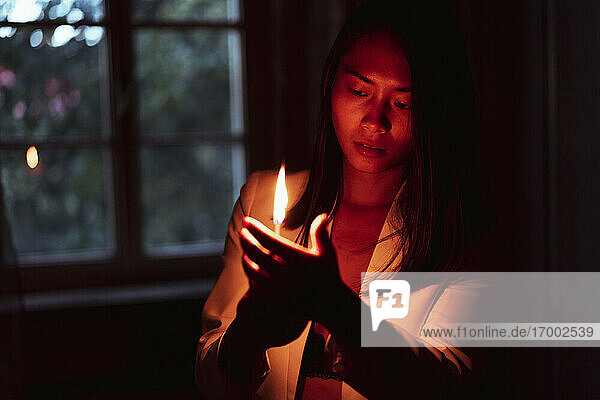 Frau hält helles brennendes Streichholz  während sie im Dunkeln zu Hause steht