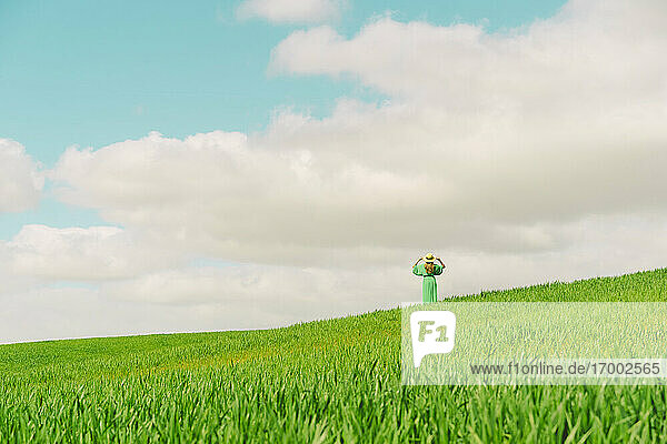 Rückenansicht einer Frau in grünem Kleid und Sommerhut  die auf einem Feld steht