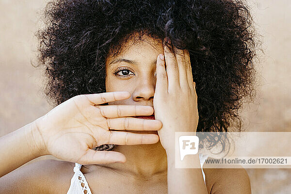Black woman staning in front of wall  covering one eye and mouth with hands