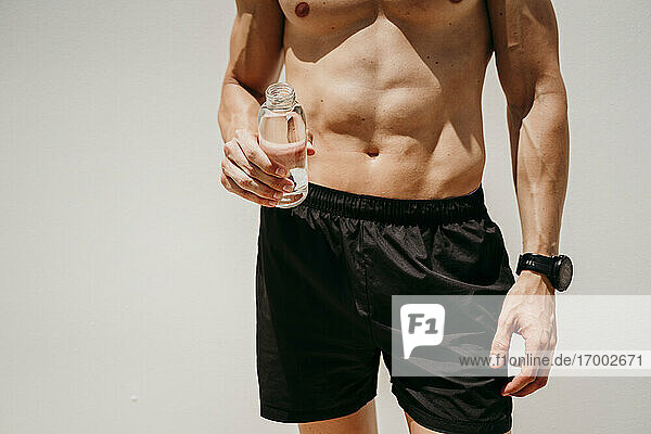 Männlicher Athlet mit nacktem Oberkörper  der eine Wasserflasche hält